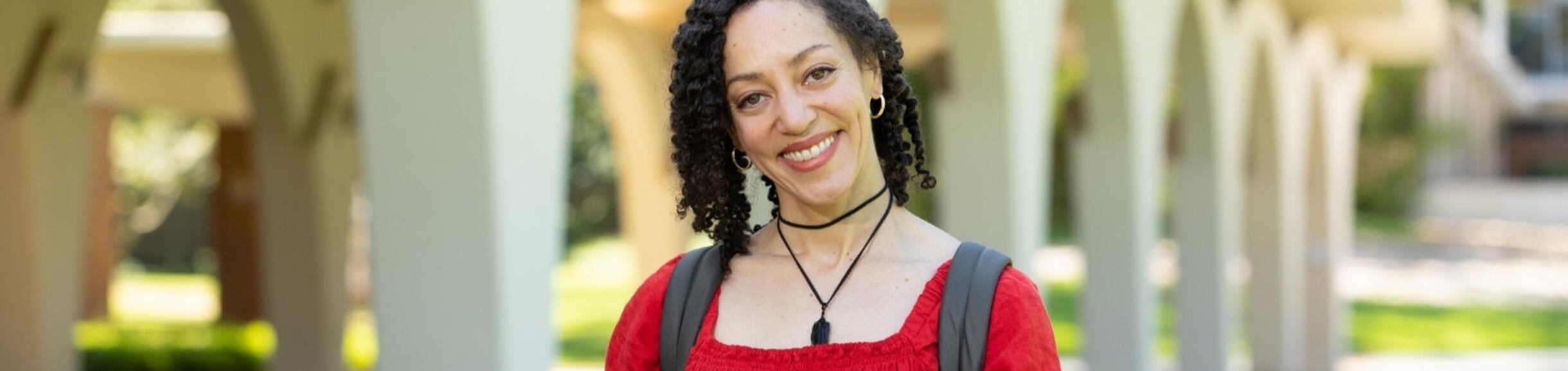 smiling woman in red dress holds a laptop in front of library