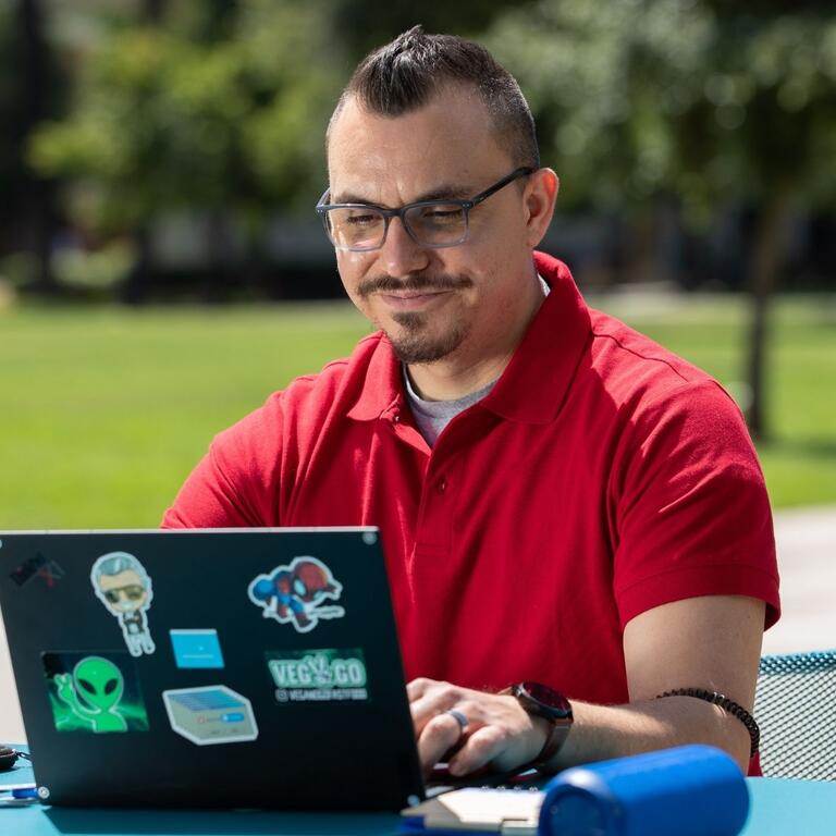 Man in red shirt uses laptop outdoors.