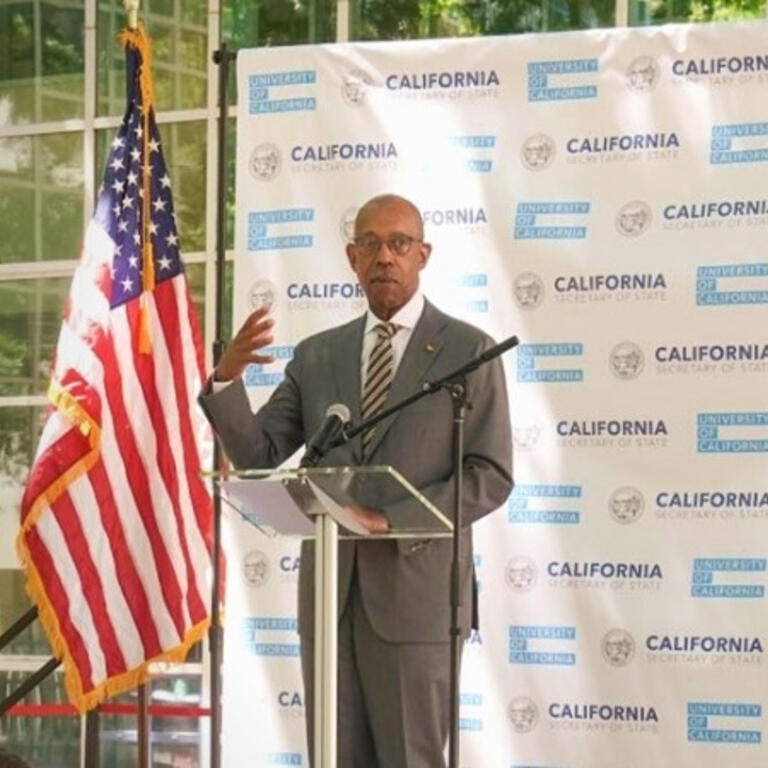 University of California President Drake is standing behind a podium giving a speech