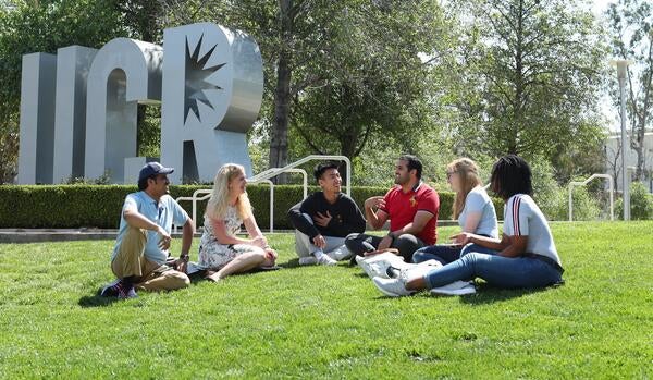 A group of students sitting on the grass by UCR letters