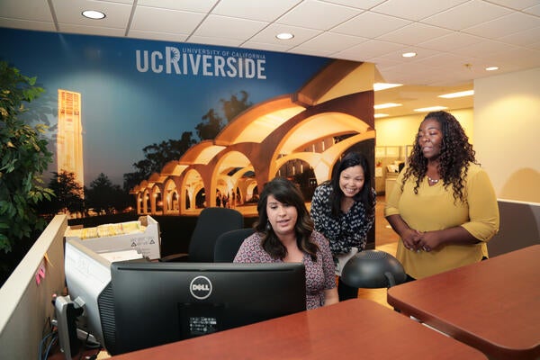 Three women standing by computer at a front desk