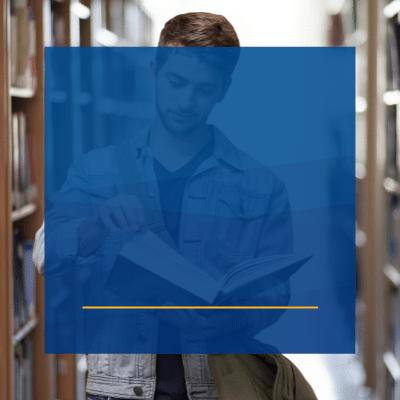 student in jean jacket reads through book in library