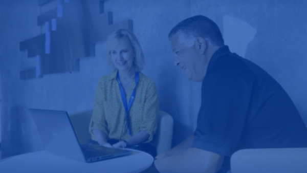 Two employees gathered by a laptop and smiling