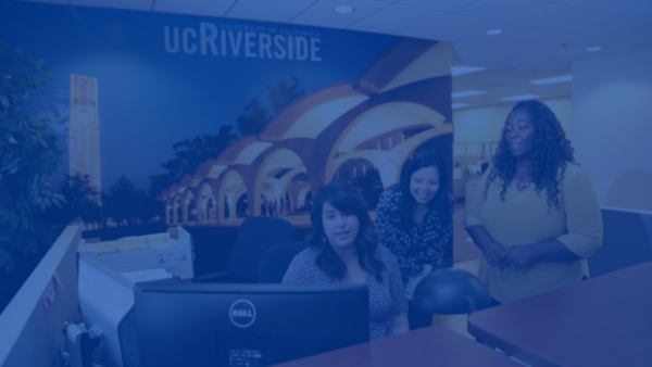 Three women standing by computer at a front desk