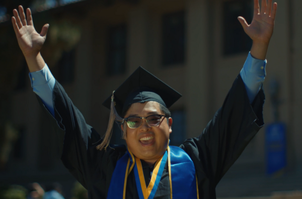 Student in cap and gown with his hands up celebrating