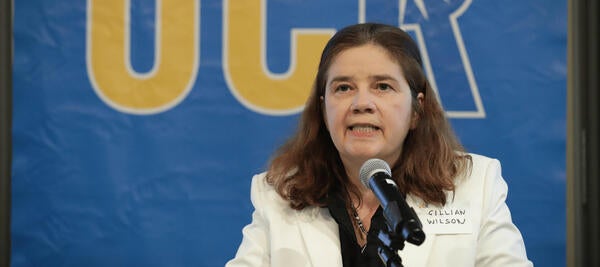 A woman with brown hair in a lab coat speaking into a microphone