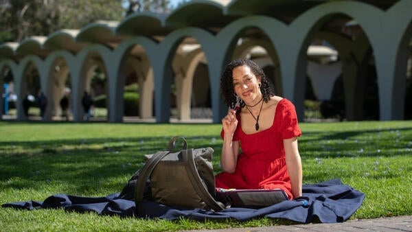 A student in red dress on lawn smiles at camera