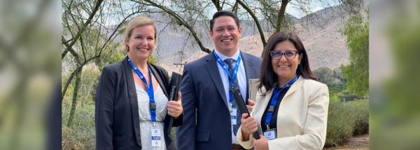 Three ITS staff members holding their laptops and smiling