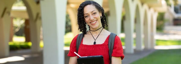 smiling woman in red dress holds a laptop in front of library