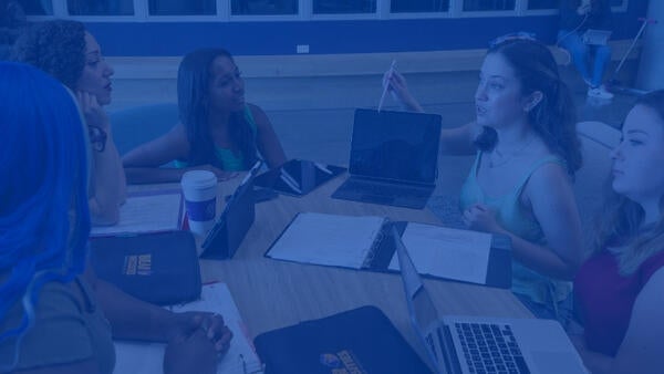 A group of students sitting together at a table and talking in front of their technology