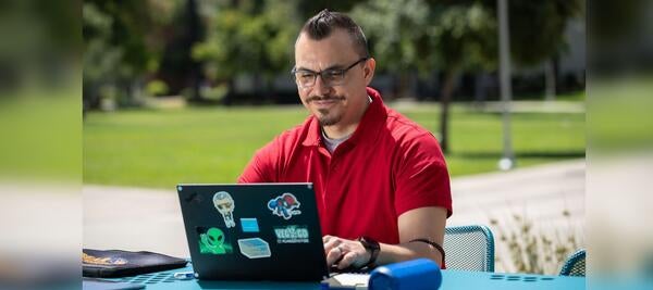 Man in red shirt uses laptop outdoors.