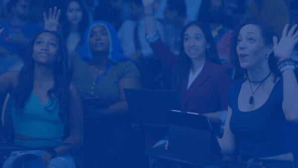 Four smiling female students raise their hands in new classroom 