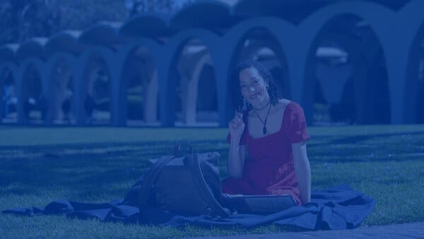 A smiling woman in red dress sits on lawn reading a book