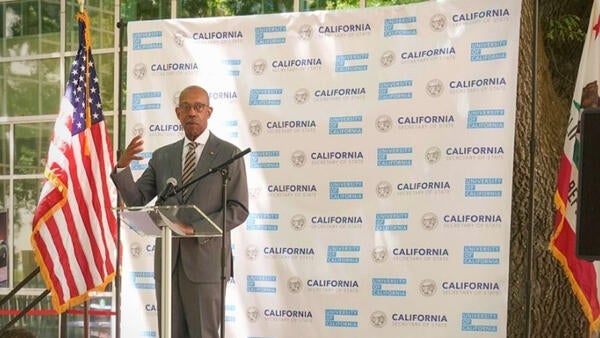 University of California President Drake is standing behind a podium giving a speech